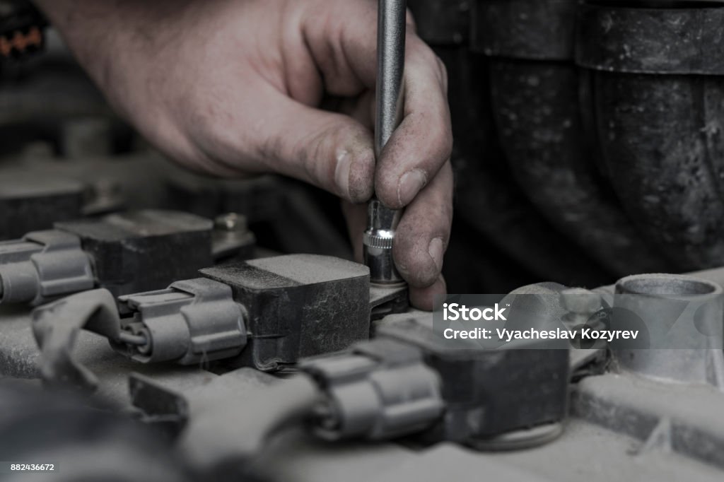 Car engine repair. Replacing the spark plugs in the engine. Repair of the old machine. Checking the ignition system is finished. The key wrench in the hand of the auto mechanic. Repair of the old machine. Auto Repair Shop Stock Photo