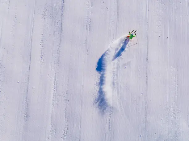 skier skiing on an empty ski-slope from drone perspective from straight above skis covered by snow no ski tracks visible on fresh prepared ski-piste
