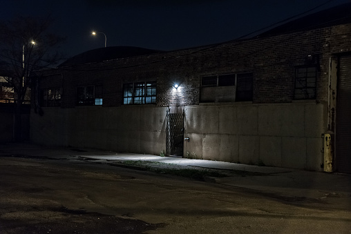 Dark scary alley at night with gated door warehouse entrance.