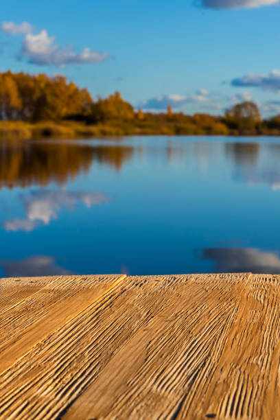 istock Empty rustic wood table top on  blurred colorful autumn landscape background with fall forest and blue sky with cloudscape reflection on the lake. Can montage or display your products 882444112