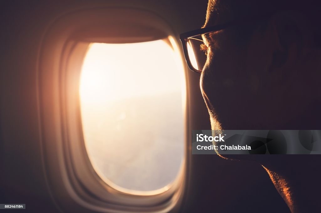 Traveling by airplane Young passenger looking out through window of the airplane during sunrise. Airplane Stock Photo