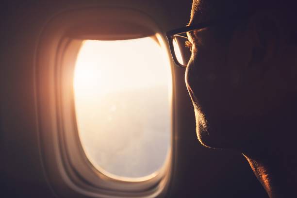 Traveling by airplane Young passenger looking out through window of the airplane during sunrise. economy class stock pictures, royalty-free photos & images
