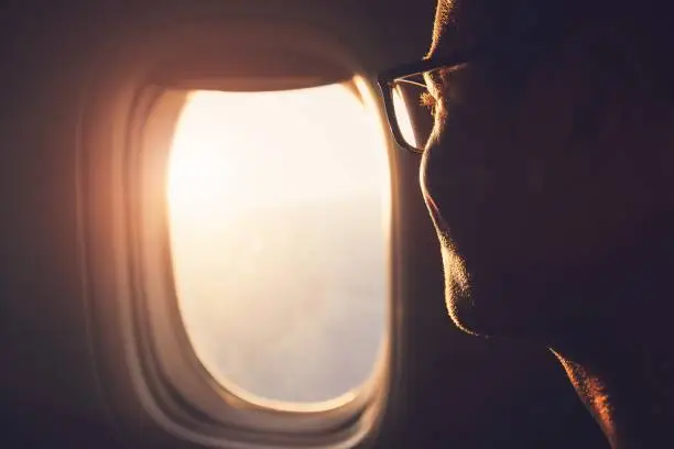 Young passenger looking out through window of the airplane during sunrise.