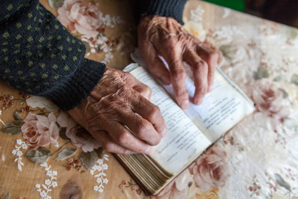 istock Old woman hands on the open prayer book. 882465046