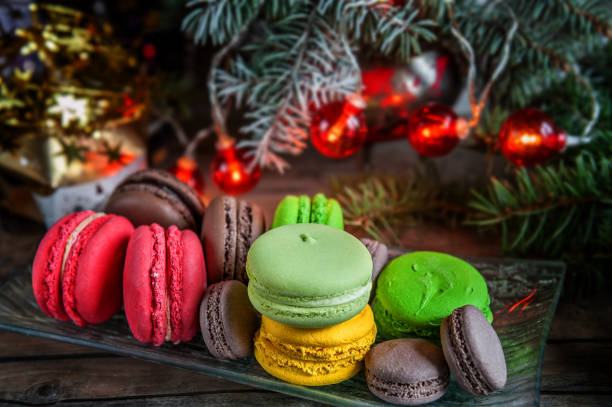 Fresh red macaroons at the Christmas table with the garland on the Christmas tree branches. Selective focus.