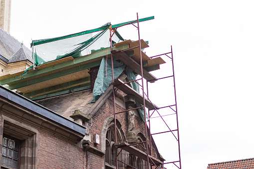 Scaffolding and boards at a construction site for restoring the roof a monumental church with a sculpture of Virgin Mary in Antwerp, Belgium