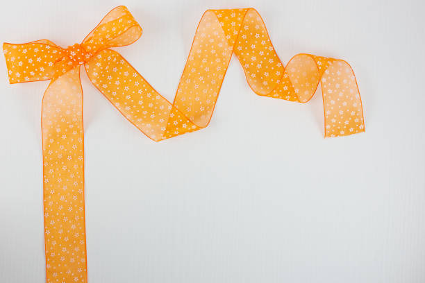 istock Orange bow with white flower on white wooden background 882494484