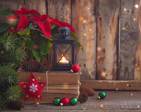 Christmas postcard with Poinsettia on the old books with fir tree, cones and toys balls and burning lantern. Toned.