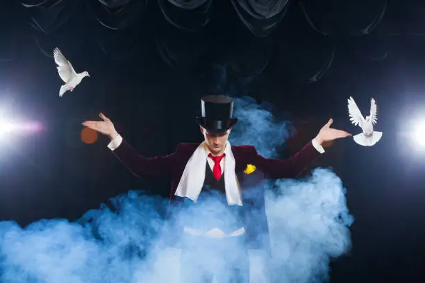 Photo of The magician with a two flying white Doves. on a black background shrouded in a beautiful mysterious smoke