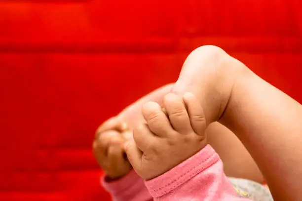 Stock photo of 5 months old baby girl who is holding het feet while lying on her back.