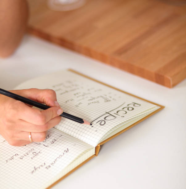 istock Happy beautiful woman standing in her kitchen writing on a notebook at home 882557960