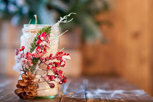 White candle holder decorated with pine cone and red ashberry on wooden table