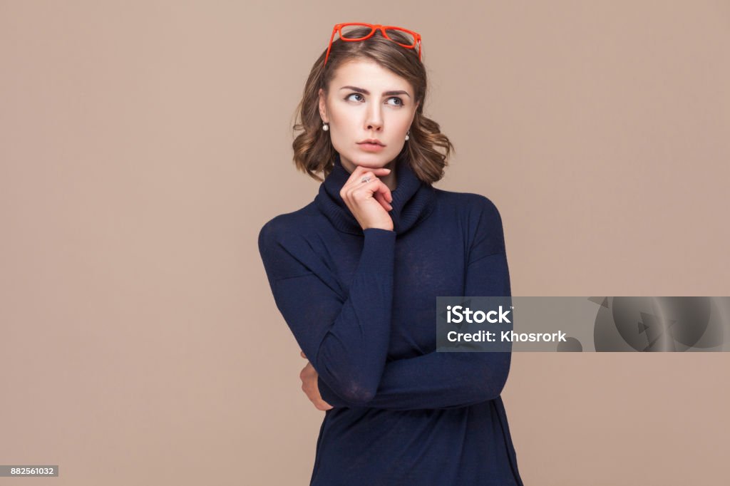 Thoughtful lady pondering and touching chin. Thoughtful lady pondering and touching chin. Studio shot, light brown background Women Stock Photo