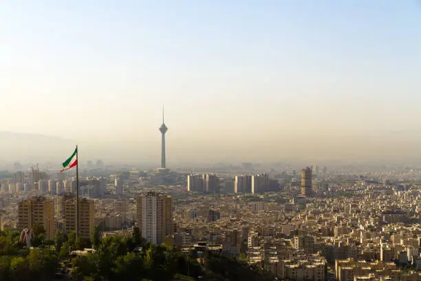 Tehran city skyline with Iranian flag and Milad Tower (Borj-e Milad landmark, hight 435 m.), seen from northern Theran. Due to heavy traffic and dense population (ca. 15 million) this capital city suffers almost daily from a yellow layer of smog.