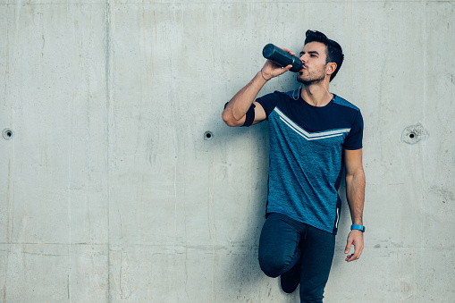 Attractive sportsman drinking water in front of a wall.