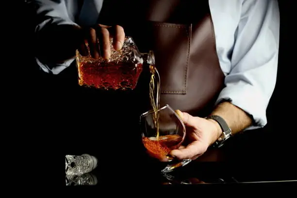a man pours cognac into a glass at the bar counter