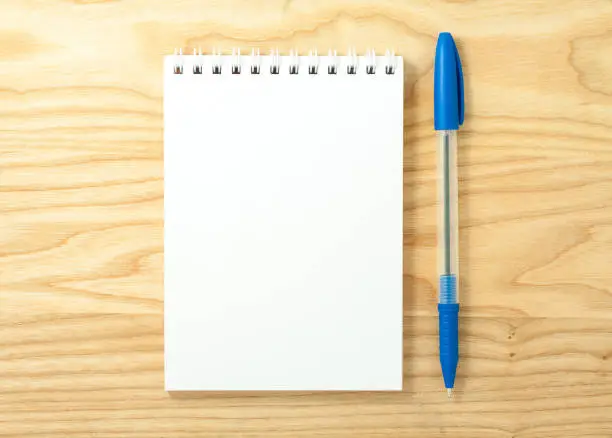 Top view of open spiral blank notebook with pen on wood desk background