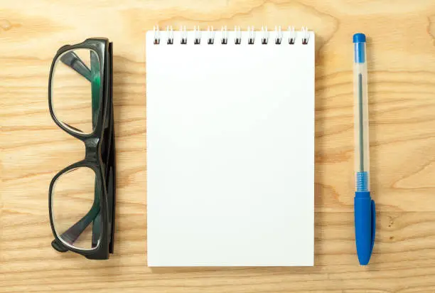 Top view of open spiral blank notebook, glasses and pen on wood desk background
