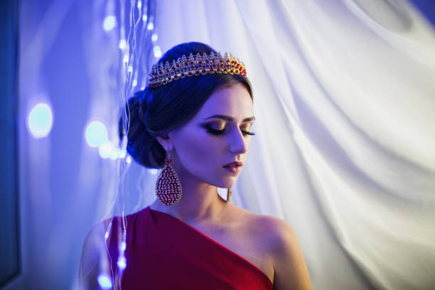 morena chica en un vestido rojo con hermoso peinado, pendientes de perlas y una corona en su cabeza y brillante maquillaje. estilo femenino. misteriosa mujer. luz azul - traje de reina egipcia fotografías e imágenes de stock