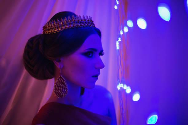 morena chica en un vestido rojo con hermoso peinado, pendientes de perlas y una corona en su cabeza y brillante maquillaje. estilo femenino. misteriosa mujer. luz azul - traje de reina egipcia fotografías e imágenes de stock