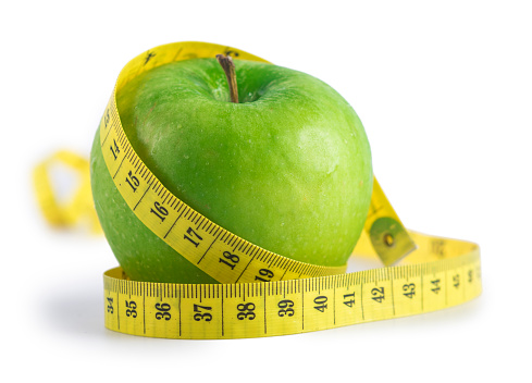 Isolated on a pure white background, diet and healthy eating concept with a green apple wrapped with a yellow measuring tape. Studio shot in macro mode.