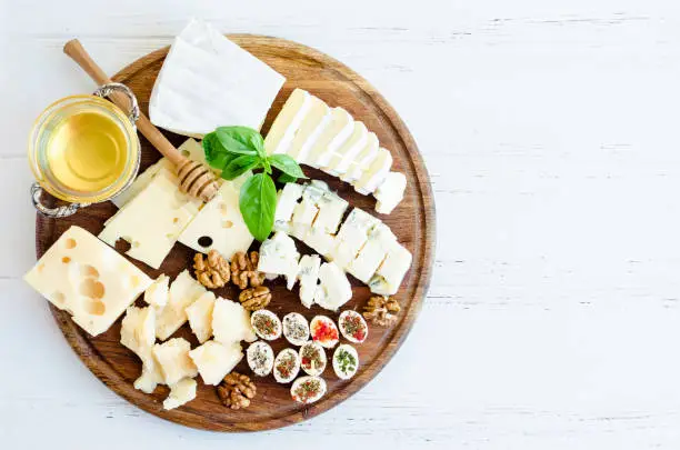 Cheese platter: Parmesan, cheddar, gouda, gorgonzola, brie and other with walnuts and honey on wooden board on white background. Tasty appetizers with different kind of cheese. Top view. Copy space.