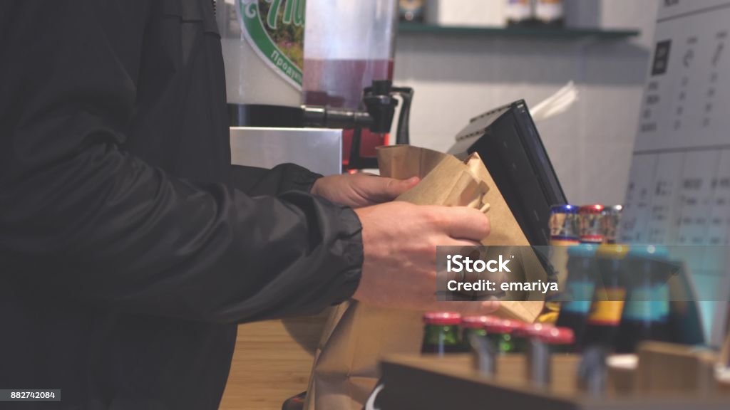 Close up of male hands putting burgers into bag. Man buys packaged food in cafe. Hands putting burgers into bag. Man buys packaged food in a cafe. Cauliflower Stock Photo