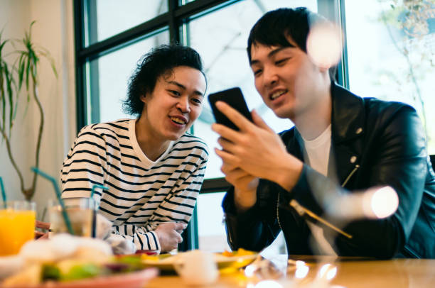 deux jeune homme regardant smartphone en riant - le monde des cafés photos et images de collection