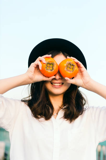 Young woman holding persimon kakis over eyes