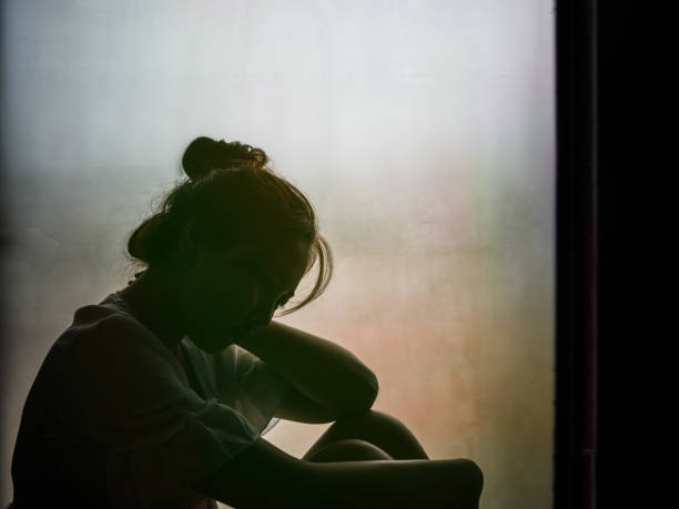 vintage filtré sur la silhouette de fille déprimée assise sur la fenêtre - women depression window sadness photos et images de collection