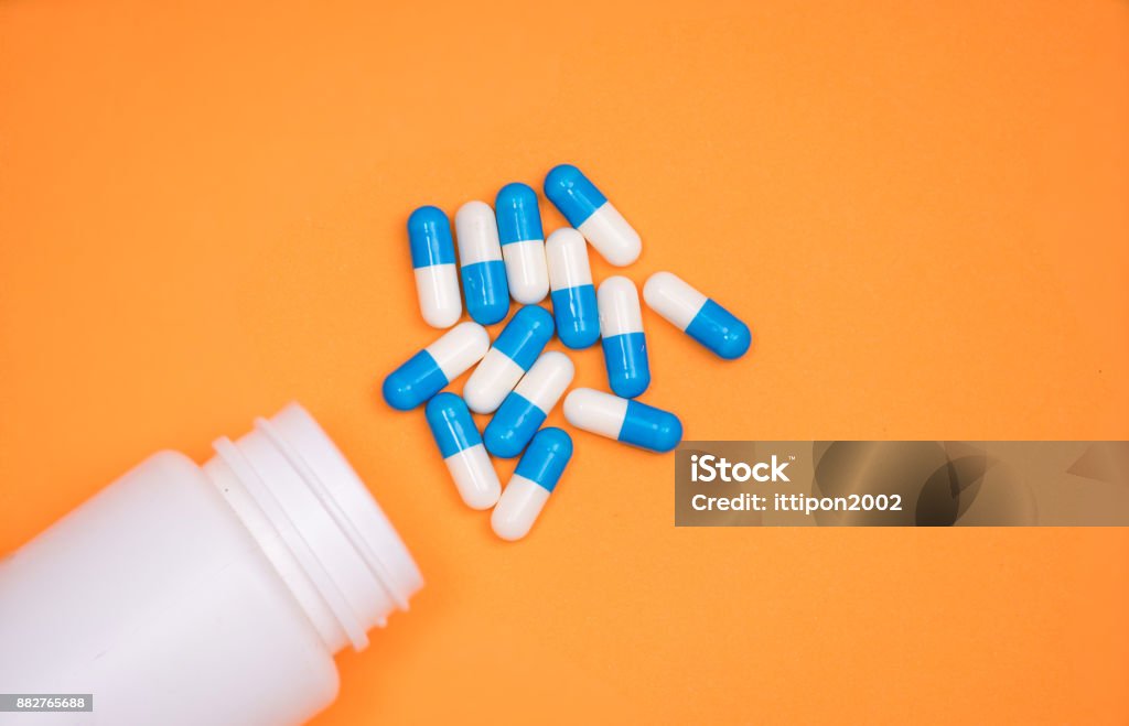 antibiotic medical drug capsule falling from bottle on  orange background Capsule - Medicine Stock Photo