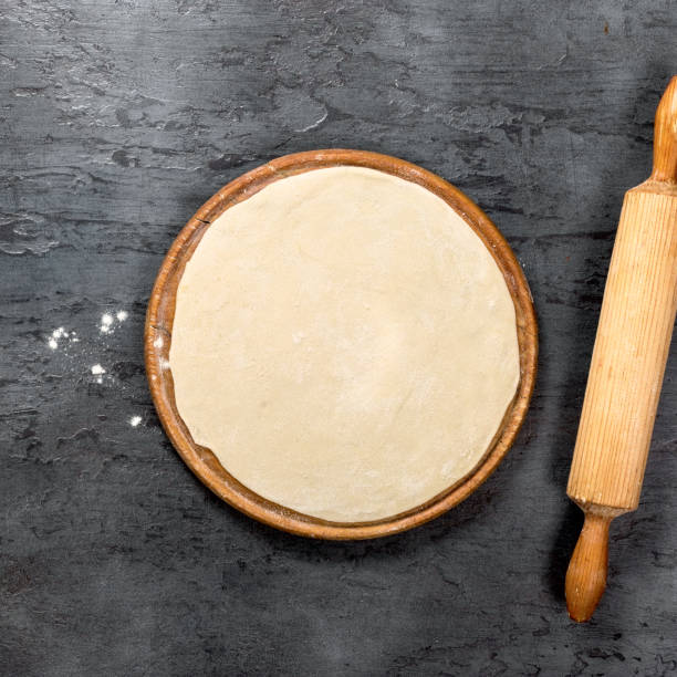 istock Pizza dough on round wooden board on a dark surface with rolling pin 882780290