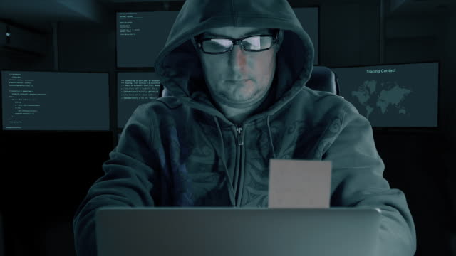 White caucasian man in hood and fashion glasses coding program for internet. Man tale stiker from monitir screen of laptop. Many monitors at backgrouns in room