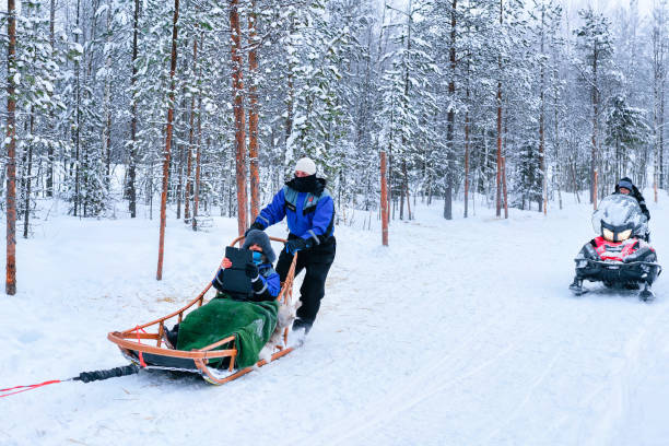 Family riding on husky dogs sledge and snowmobile in Rovaniemi Rovaniemi, Finland - March 3, 2017: Family riding on husky dogs sledge and person on snowmobile in Rovaniemi, Lapland in winter Finnish forest Snowmobiling stock pictures, royalty-free photos & images