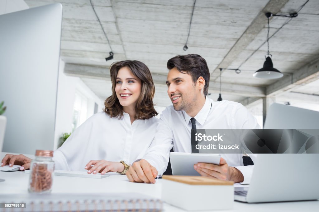 Business colleagues working together in office Business colleagues using desktop computer. Young businessman and businesswoman working together in office looking at computer screen and smiling Financial Advisor Stock Photo