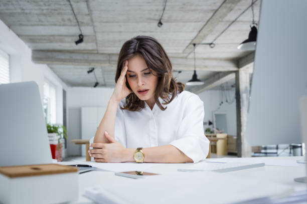 female entrepreneur with headache sitting at desk - business struggle imagens e fotografias de stock