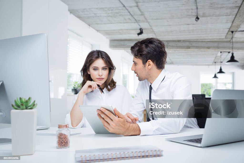 Business people working together in office Two business people working together in office. Businessman holding digital tablet and discussing with businesswoman at workplace. Contemplation Stock Photo