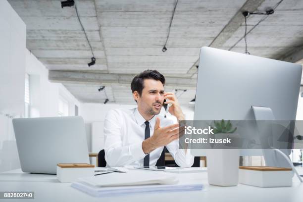 Annoyed Businessman Talking On Phone In Office Stock Photo - Download Image Now - Displeased, Anger, Men