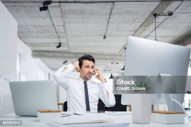 Frustrated Businessman Talking On Phone At His Desk Stock Photo - Download Image Now
