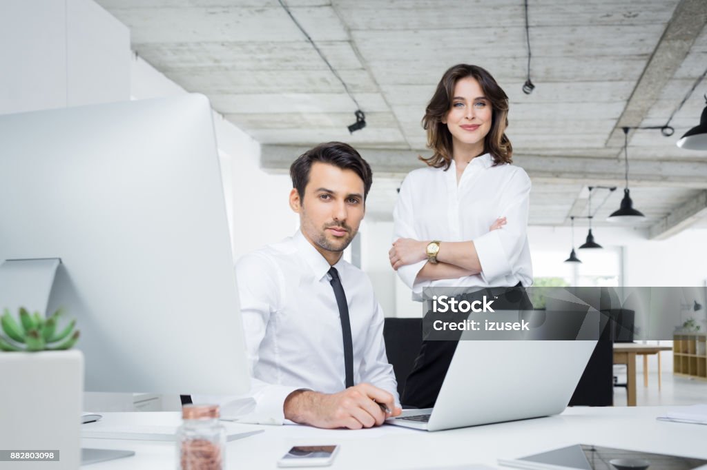 Two business partners in office Two business partners working together in office. Confident young businessman and businesswoman looking at camera. Financial Advisor Stock Photo