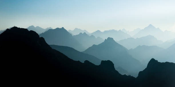 silhuetas de cadeias de montanhas espetaculares azul e ciano. cruzes visíveis do cume. - european alps scenics mist tirol - fotografias e filmes do acervo