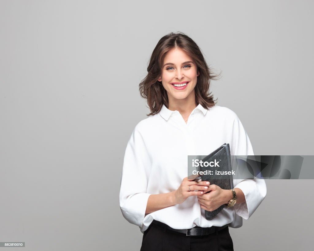 Beautiful businesswoman standing with a diary Portrait of beautiful businesswoman standing with a diary against grey background. Financial Advisor Stock Photo
