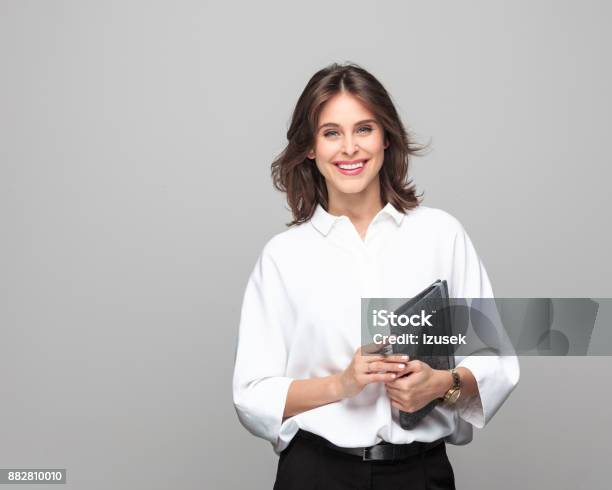 Beautiful Businesswoman Standing With A Diary Stock Photo - Download Image Now - Financial Advisor, Gray Background, Happiness