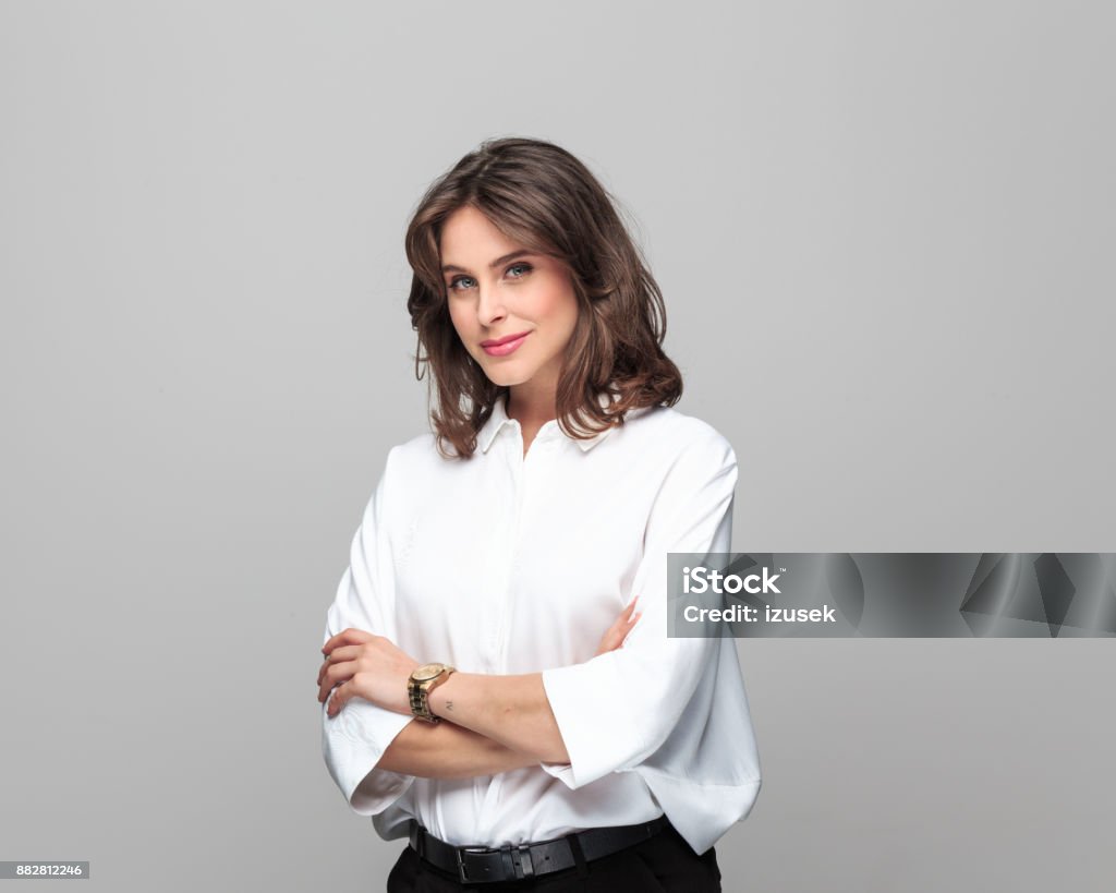 Attractive businesswoman standing with her arms crossed Portrait of attractive businesswoman standing with her arms crossed against grey background. Businesswoman Stock Photo