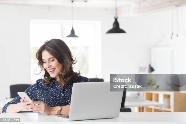 Smiling Young Woman Using Phone At Her Office Desk Stock Photo - Download Image Now - 20-24 Years, Adult, Adults Only