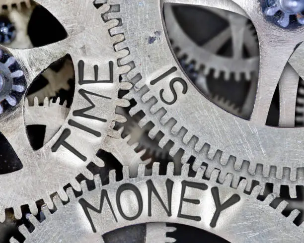 Macro photo of tooth wheel mechanism with TIME IS MONEY words imprinted on metal surface