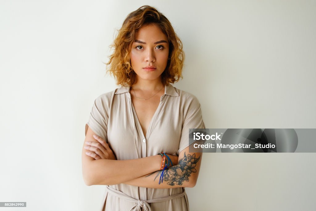 Portrait of sad or serious young woman in studio Portrait of sad or serious young Asian woman wearing dress standing with crossed arms and looking at camera in studio. Depression and stress concept Serious Stock Photo