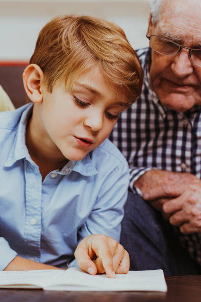 istock Diligent schoolboy reading book with grandparents 882850712