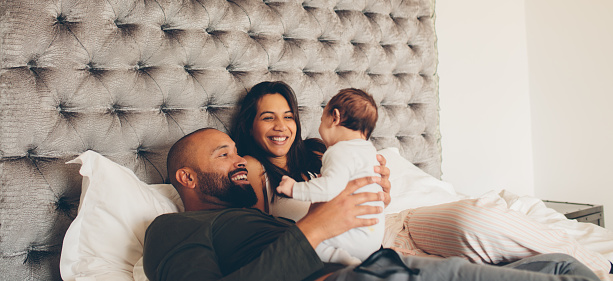 Happy parents playing with their newborn son on bed at home. Couple with little baby boy on bed.