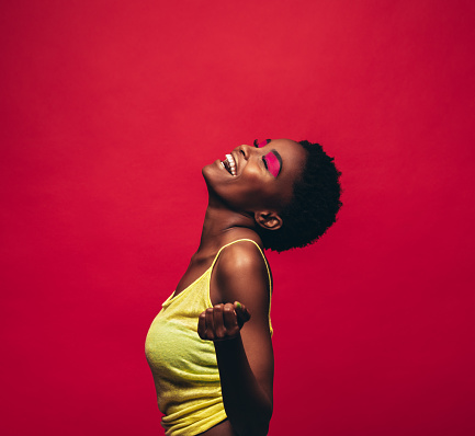 Cheerful young woman dancing over red background. African female model dancing in studio and enjoying.